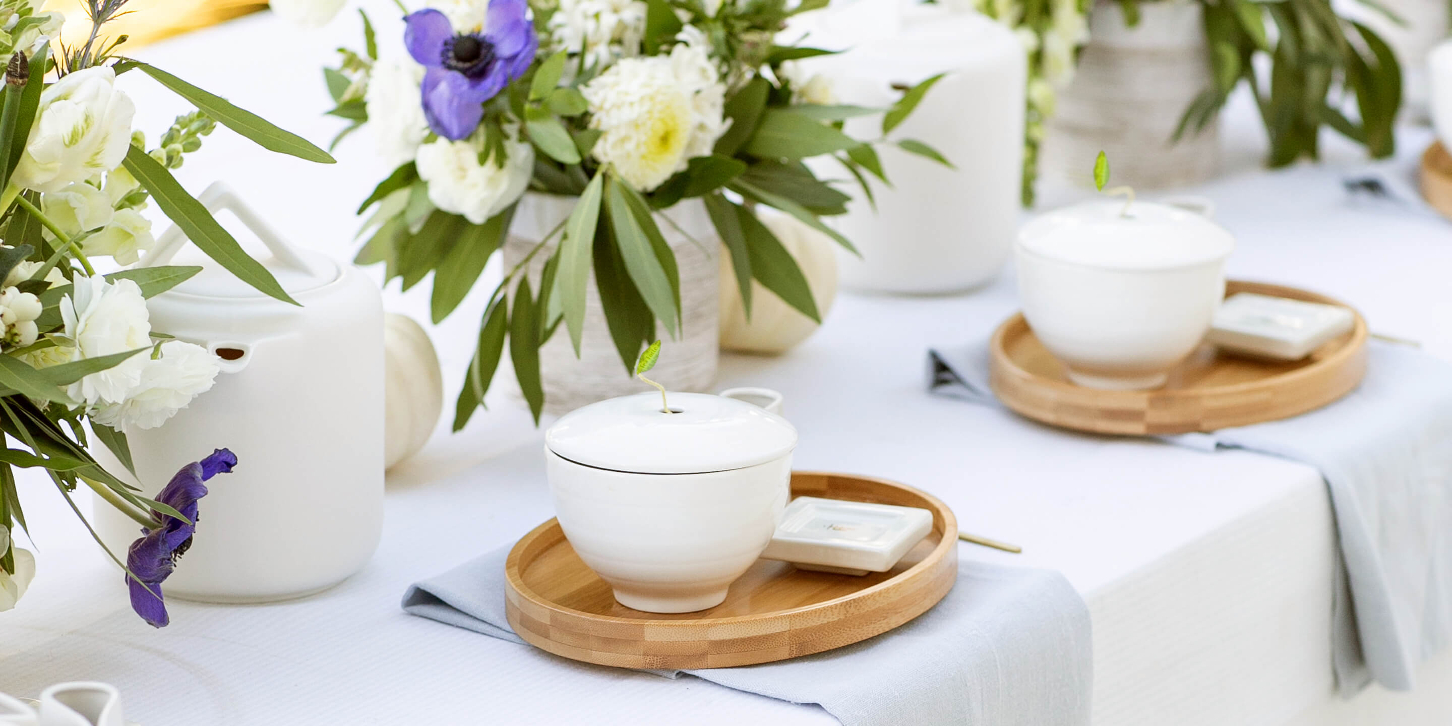 Cafe Cups and a Oval trays displayed on a long table with flower arrangements and white teapots