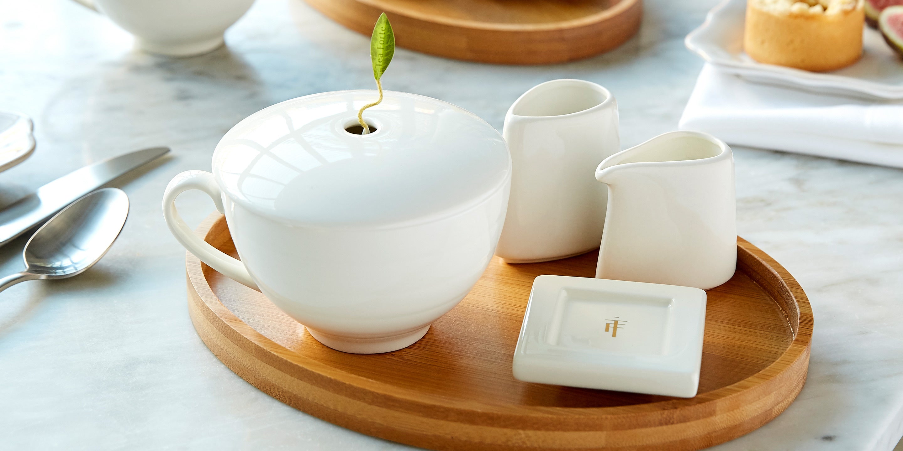 Cup Cup in white on a oval bamboo tray with a white tea tray and sugar and creamer set.