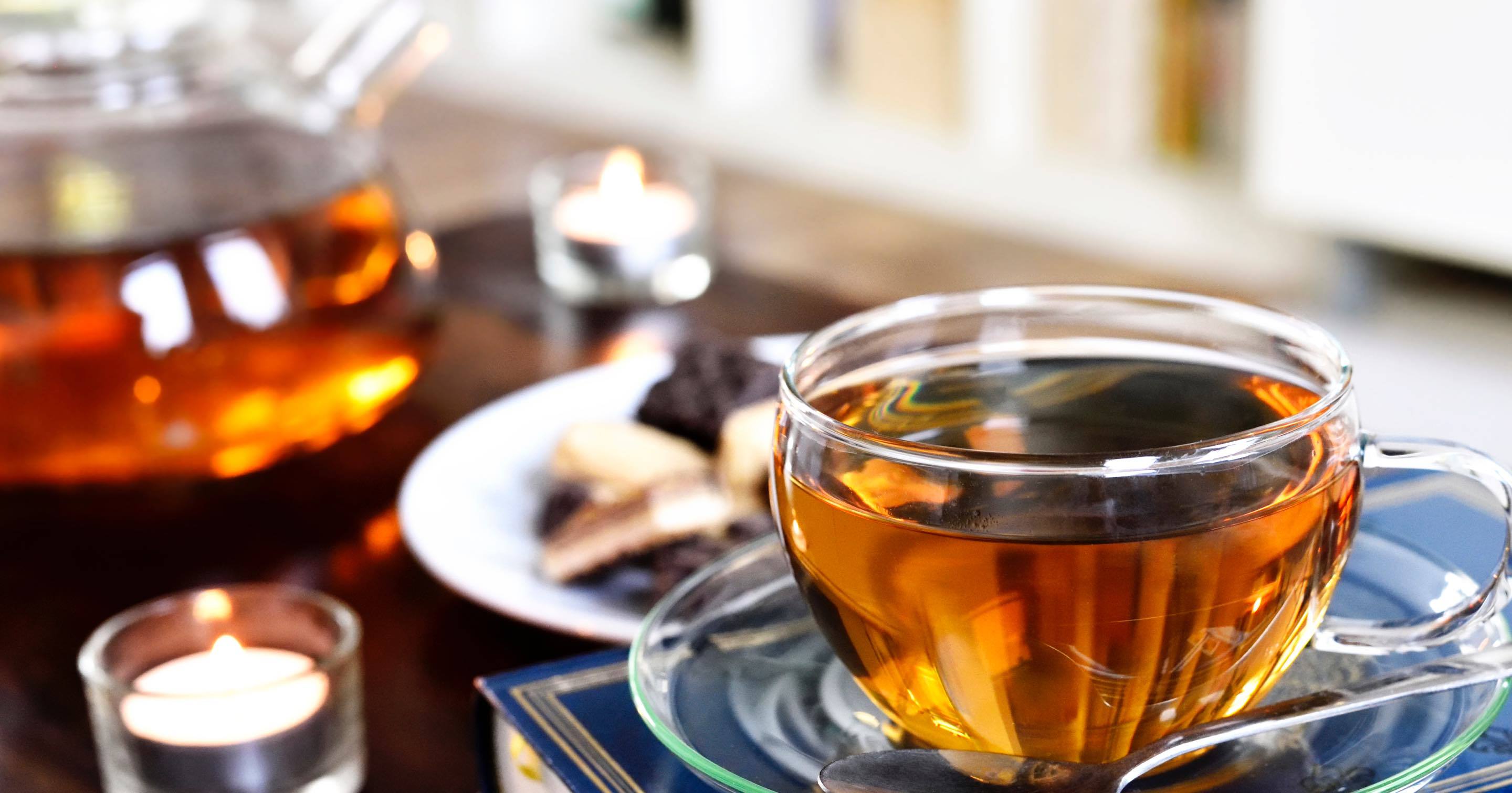 Glass cup of English Breakfast tea on a table with a glass teapot in the background