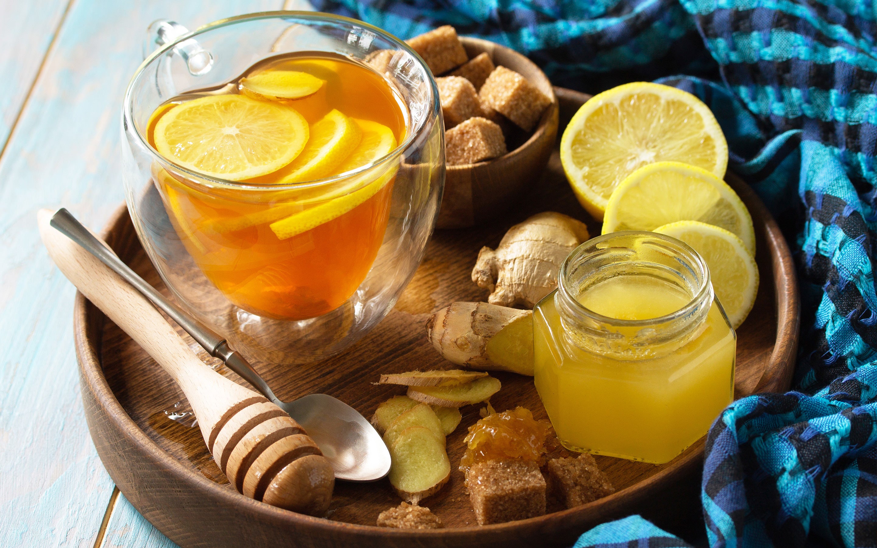 Glass mug of tea with lemon slices on a tray with honey, lemons and suagr