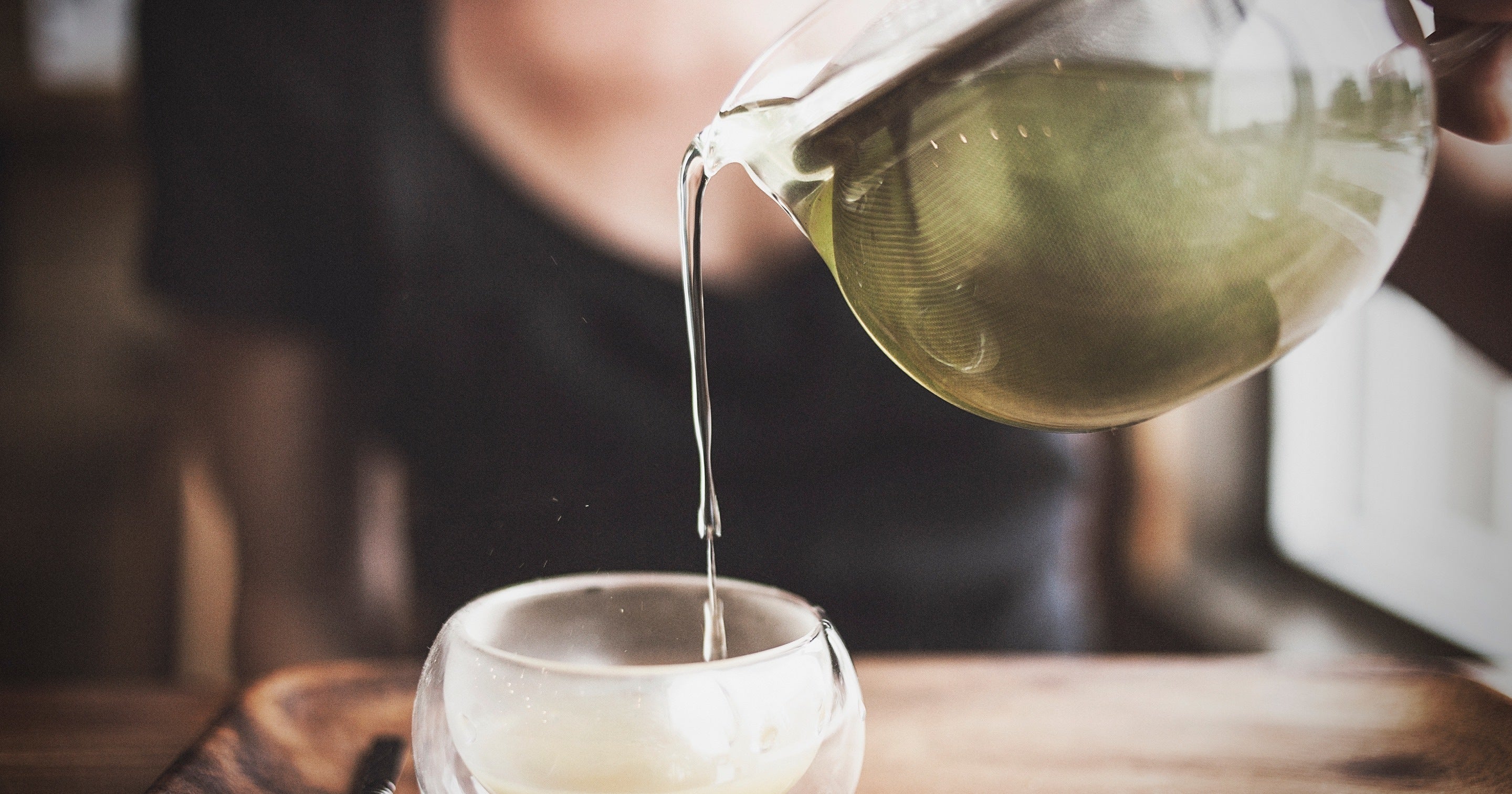 Pouring tea from a glass teapot into a small glass cup