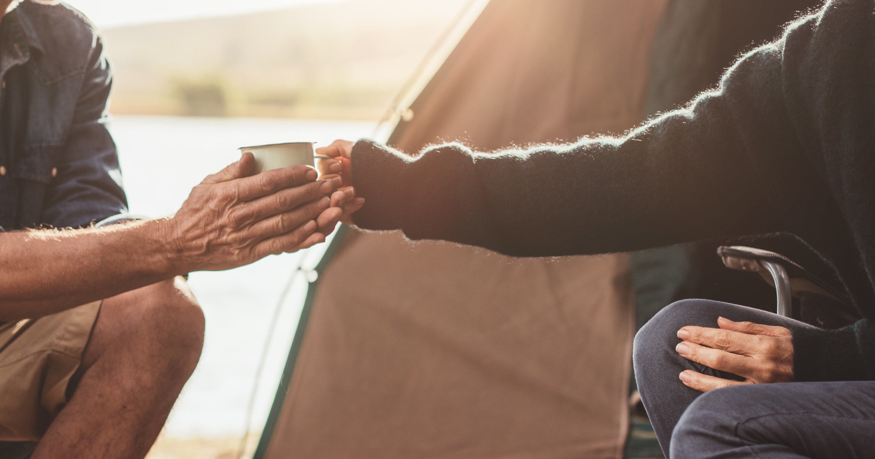 Handing someone a mug of tea in the early light by a tent