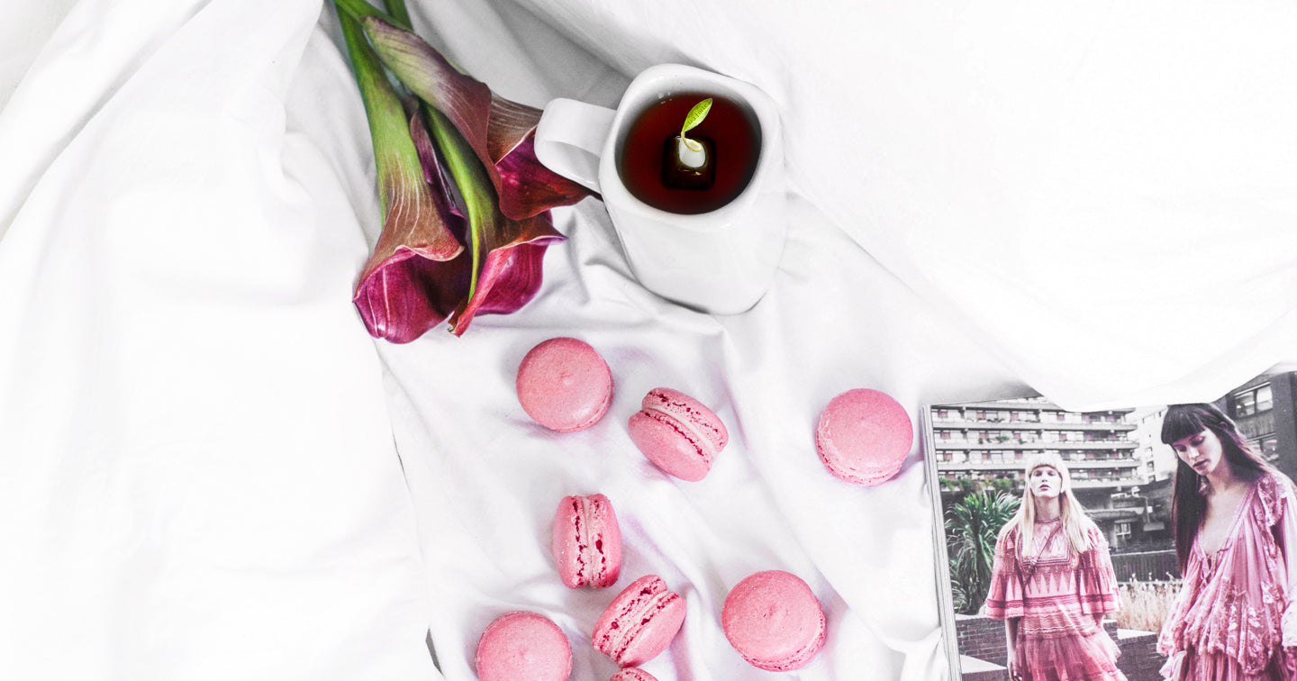 Magazine, flowers and macarons with a cup of tea on a white tablecloth