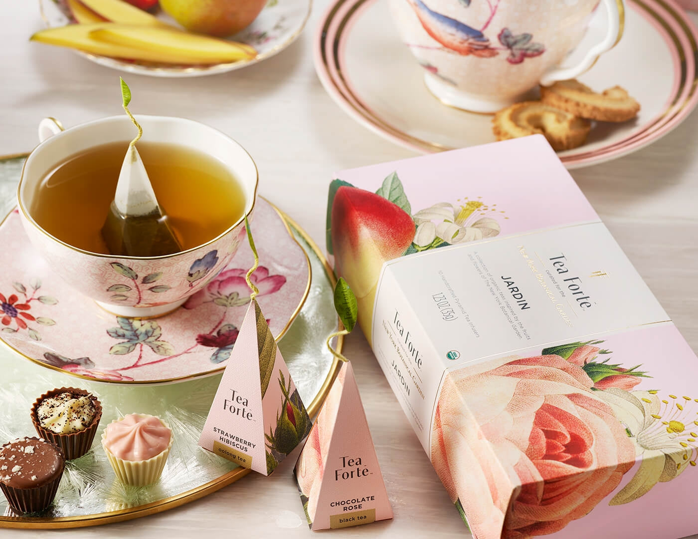 Jardin Petite Presentation Box on a table with a fancy pink teacup and saucer and mini desserts