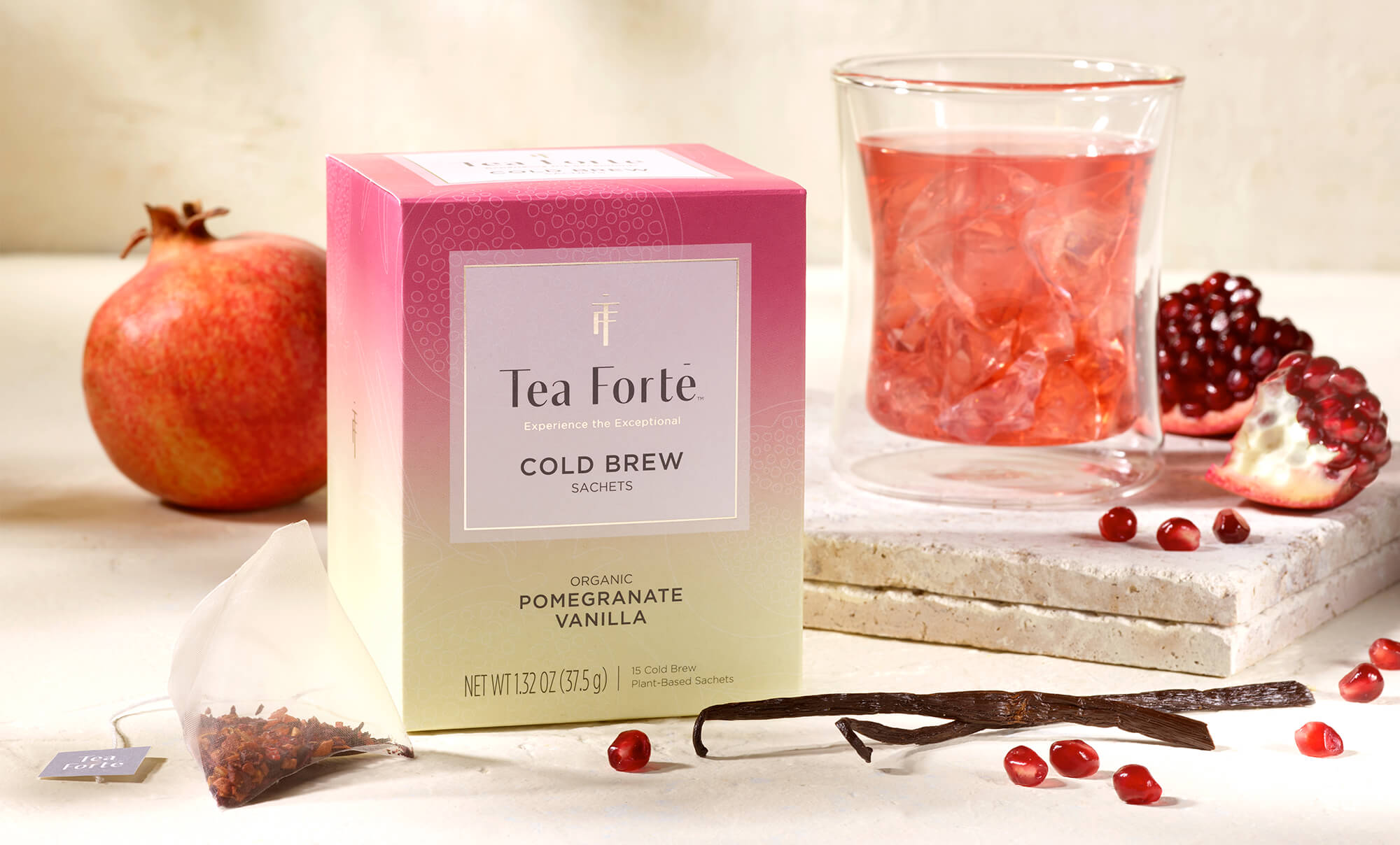 Tea Forte Pomegranate Vanilla cold brew box with a glass of tea and pomegranate fruits on a light background