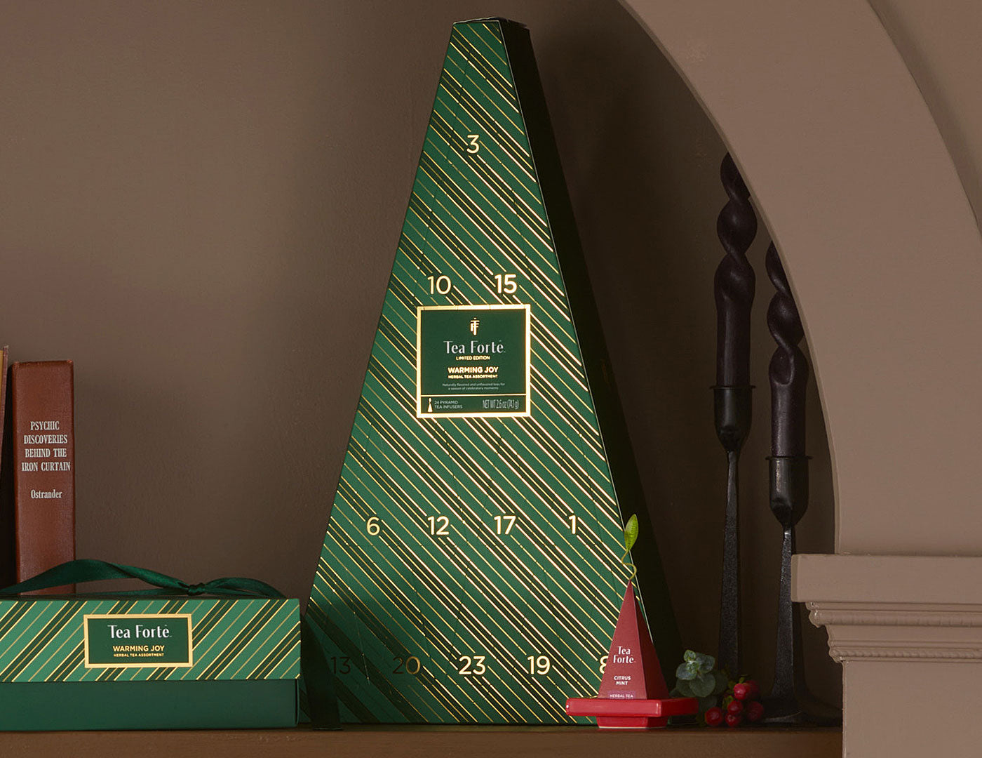 A green triangular Advent Calendar with diagonal striped pattern and gold numbers, displayed on a shelf next to a smaller matching box and decorative items.
