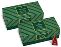 Two green Tea Forté Warming Joy Herbal Tea Presentation Boxes with gold geometric stripes and a single red pyramid tea infuser shown beside them on a white background.