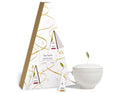 White ceramic teacup with lid and tea bag sachets displayed next to decorative gift box packaging with gold accents.