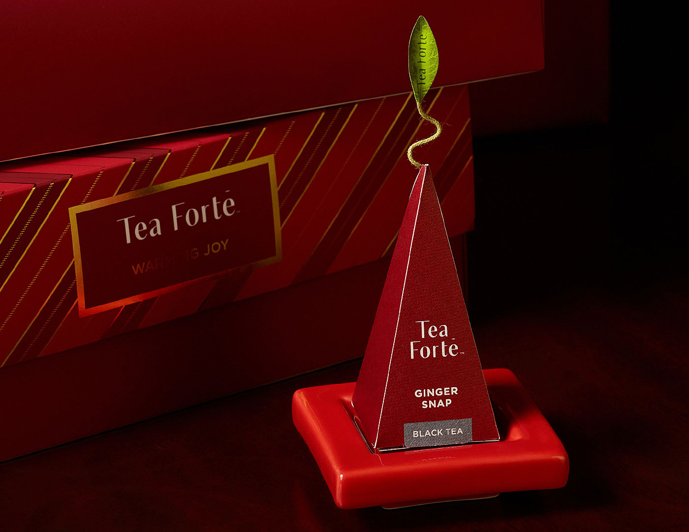 A red pyramid-shaped tea infuser on on a red Tea Tray, with a matching Petite Presentation Box in the background.