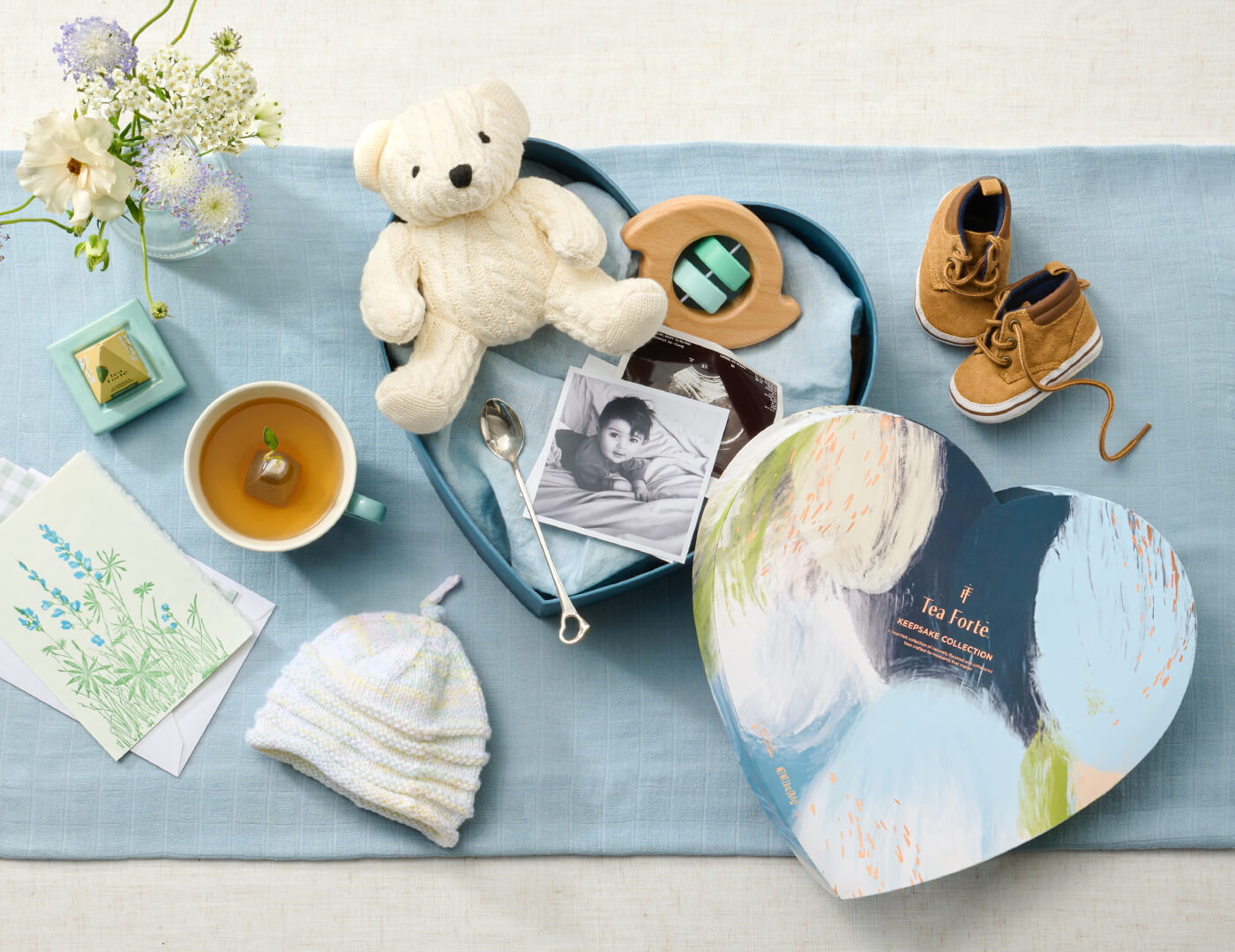 Keepsake Heart Box, Something Blue, of 26 pyramid infusers, lid open, revealing infusers, with cups of tea on a table with baby shower items