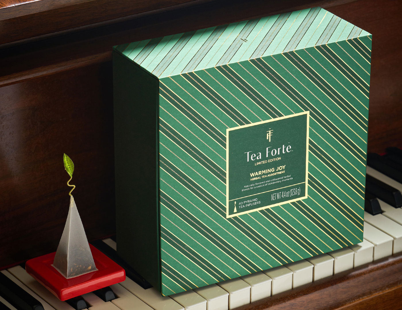 Wrming Joy Herbal Tea Chest closed, displayed on a piano next to a red Tea Tray with a tea infuser on top.