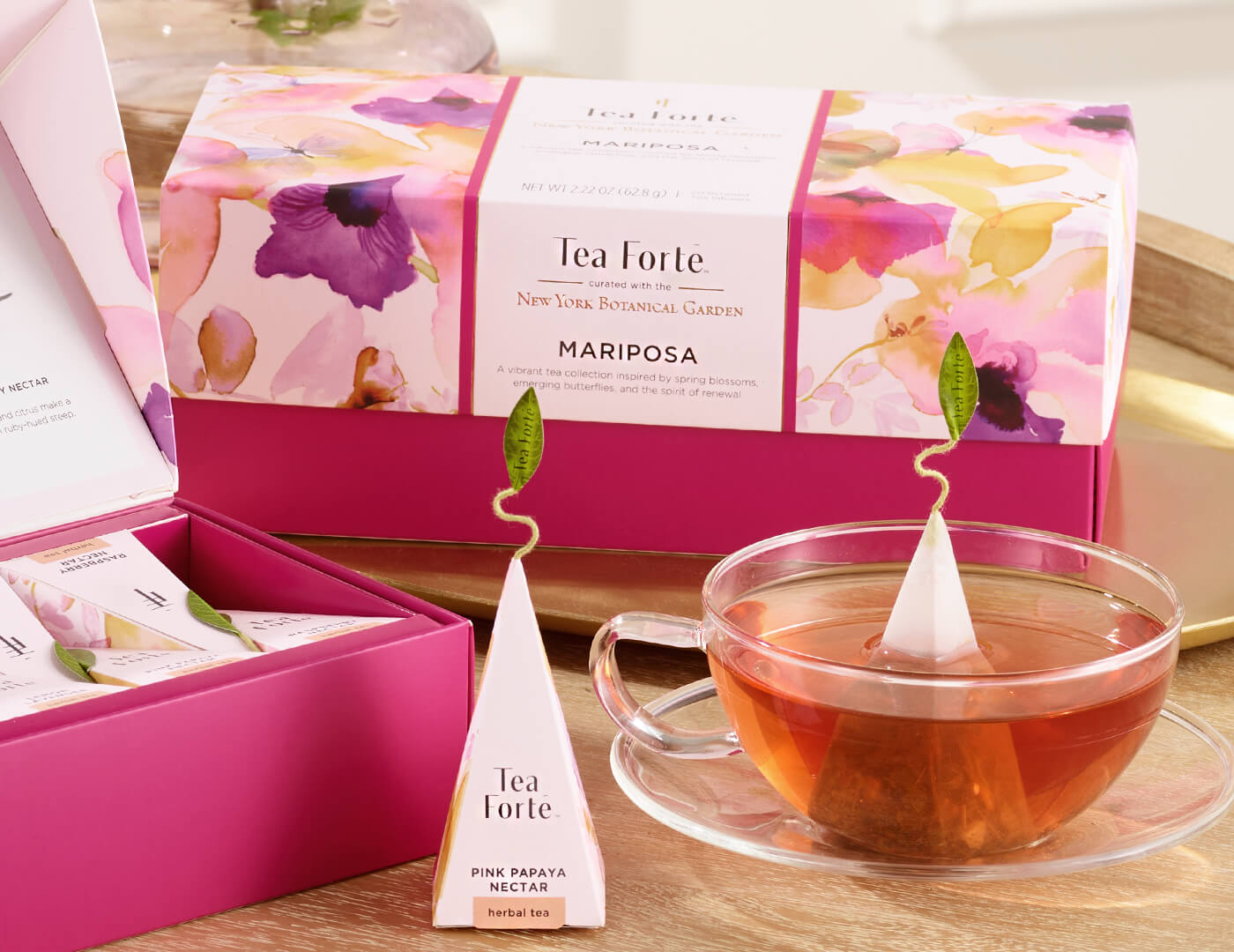  Mariposa Presentation Box of 20 pyramid tea infusers,  closed box o a table with a glass cup of tea and other boxes and infusers