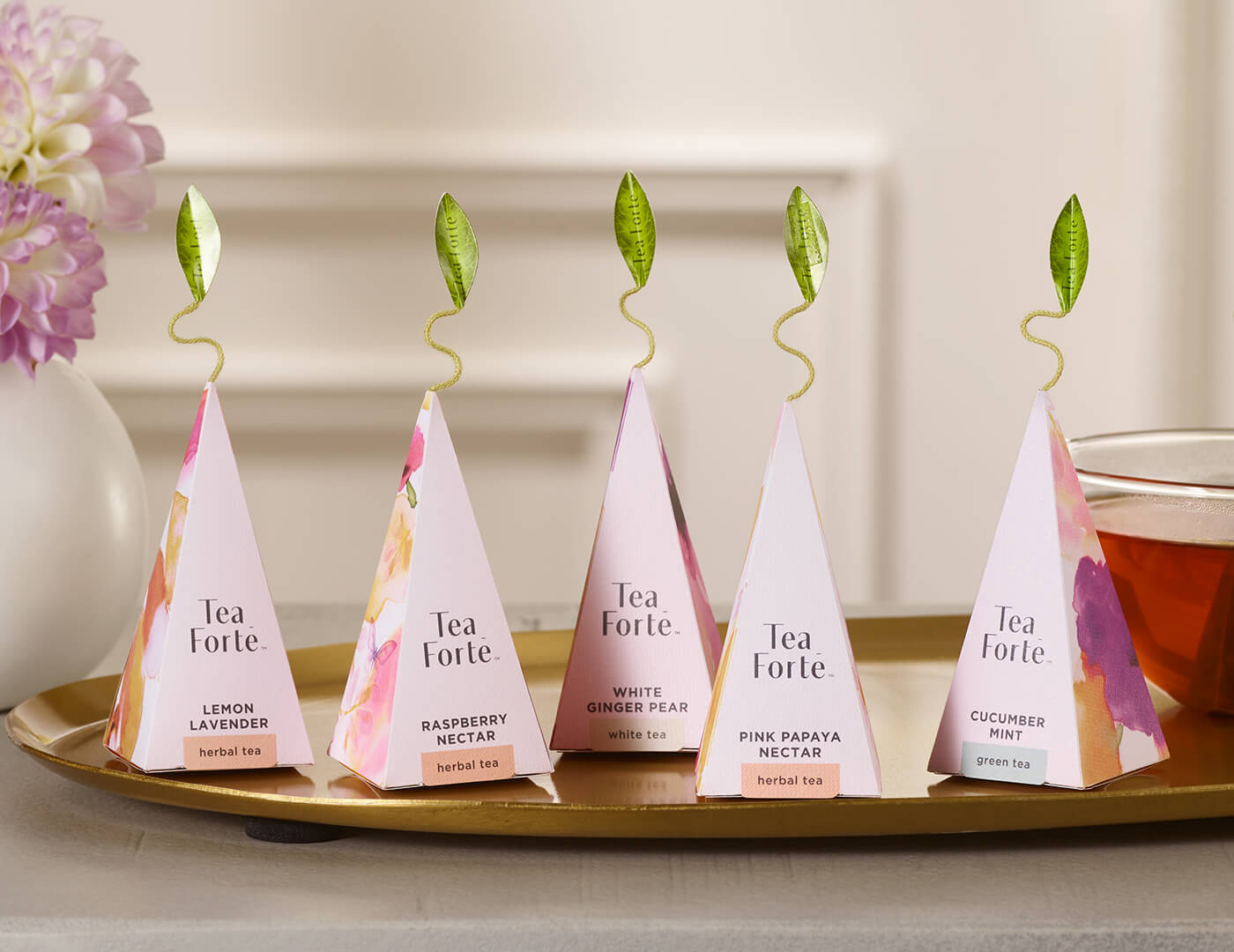 Mariposa pyramid tea infusers, on a tea tray on a table with flowers and a glass cup of tea.