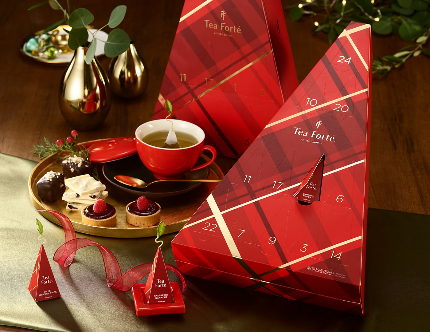 Warming Joy Advent Calendars on a festive holiday table with a red teacup, pyramid infusers and chocolate desserts.