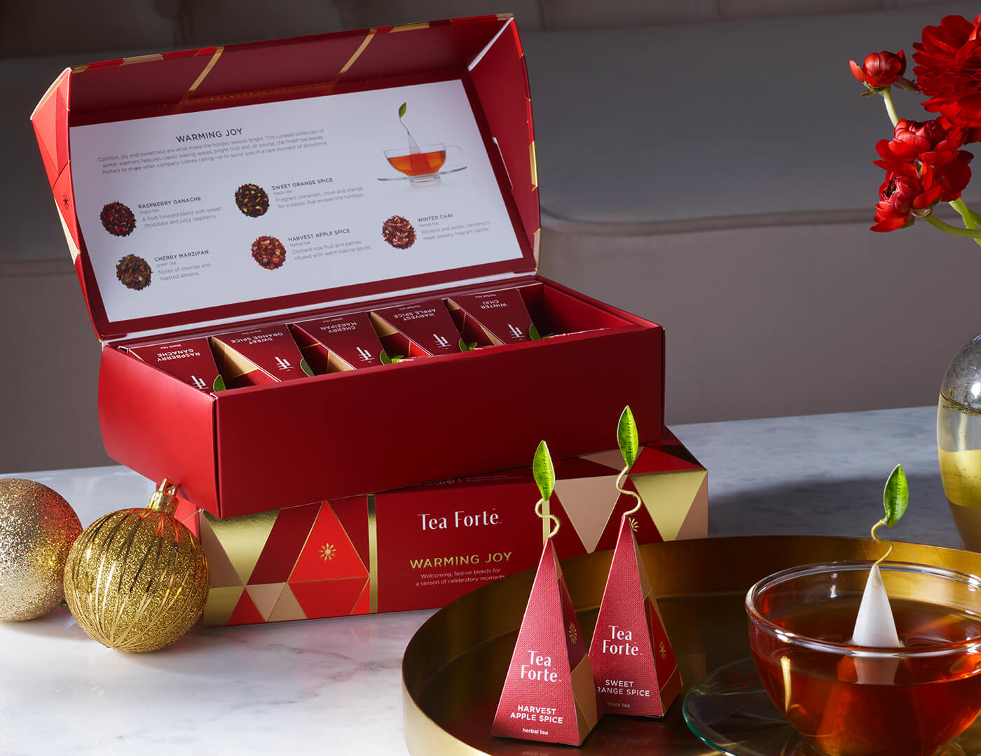 Warming Joy Petite Presentation Box, open on a table with infuser and a glass cup of tea