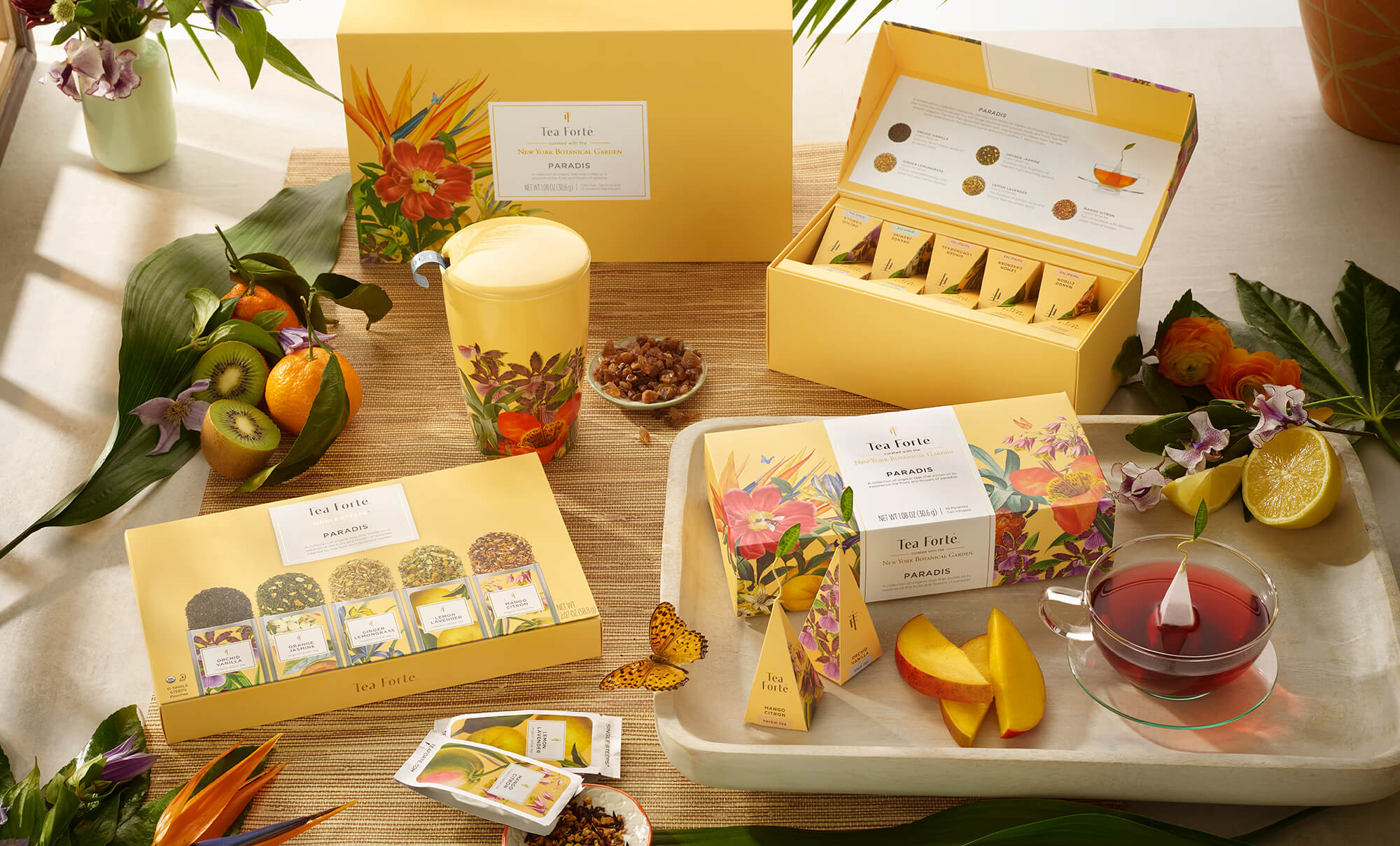 Paradis Collection on a table with fruit and butterflies